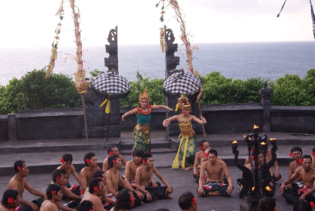 Les interprètes du kecak assis en cercle autour de deux danseuses à Uluwatu, la mer en arrière-plan